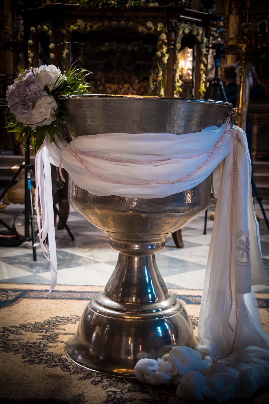 A baptism font adorned with pink floral decorations in a Nafplio church.