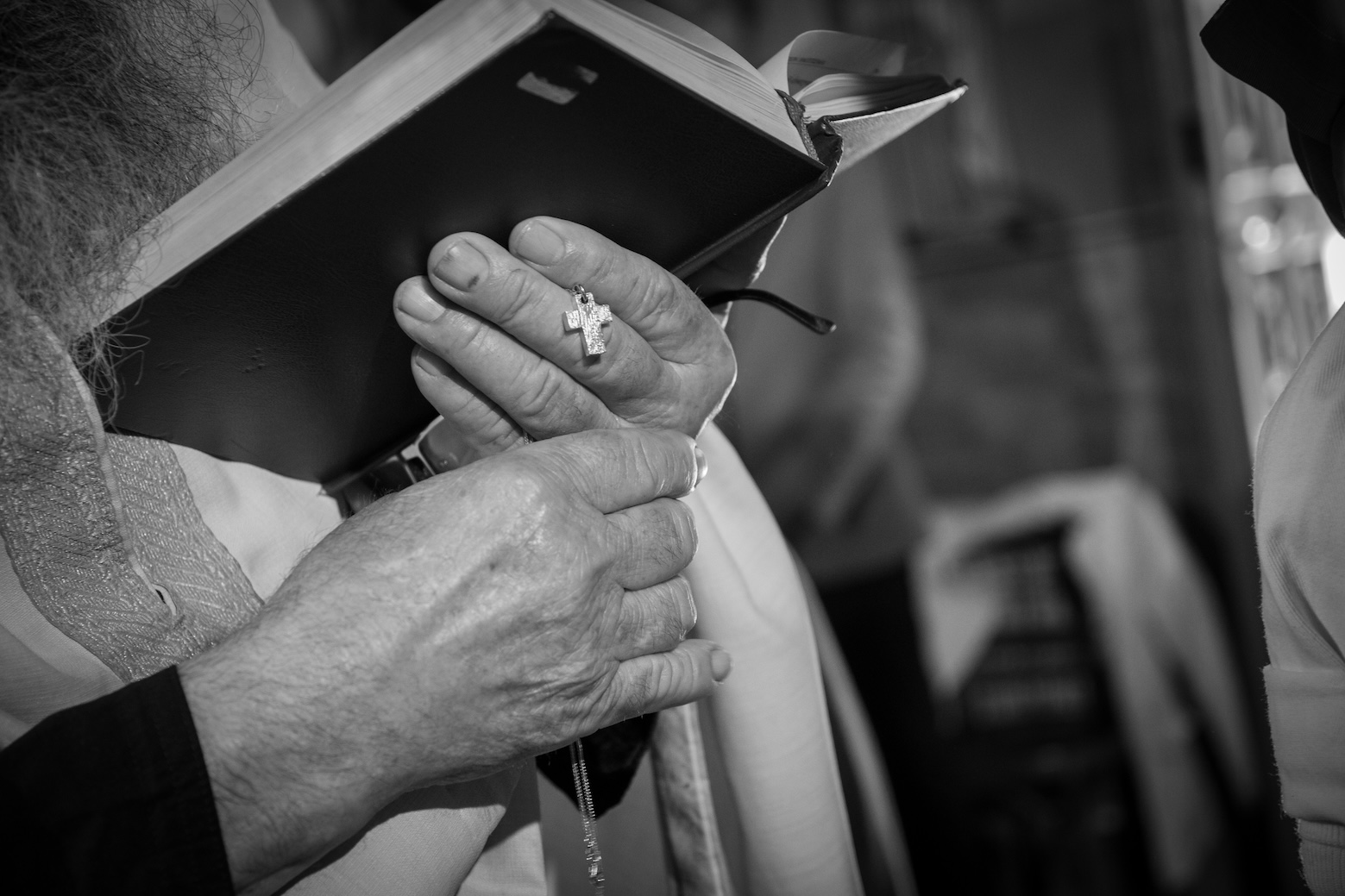 A priest holding a baptism book and a cross during a Greek church ceremony.