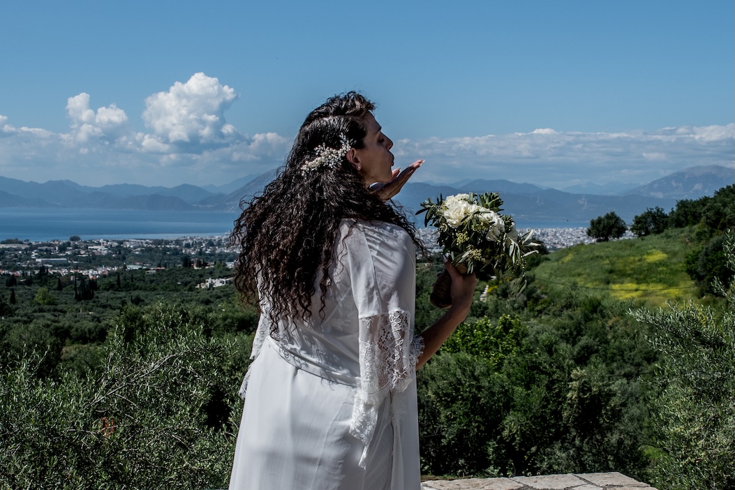 A bride standing against a Greek landscape with a sea view.